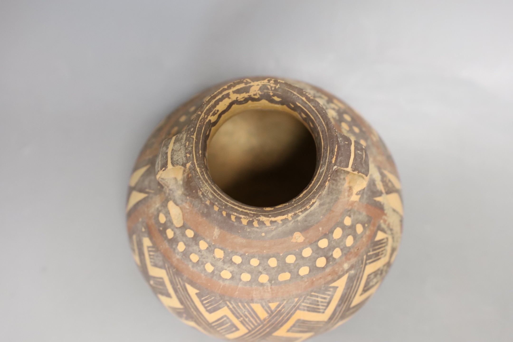 A Chinese pigment painted pottery two handled jar, possibly Neolithic, 14cm high